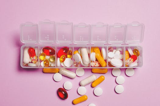 A variety of pills in a weekly pill organizer on a pink background.